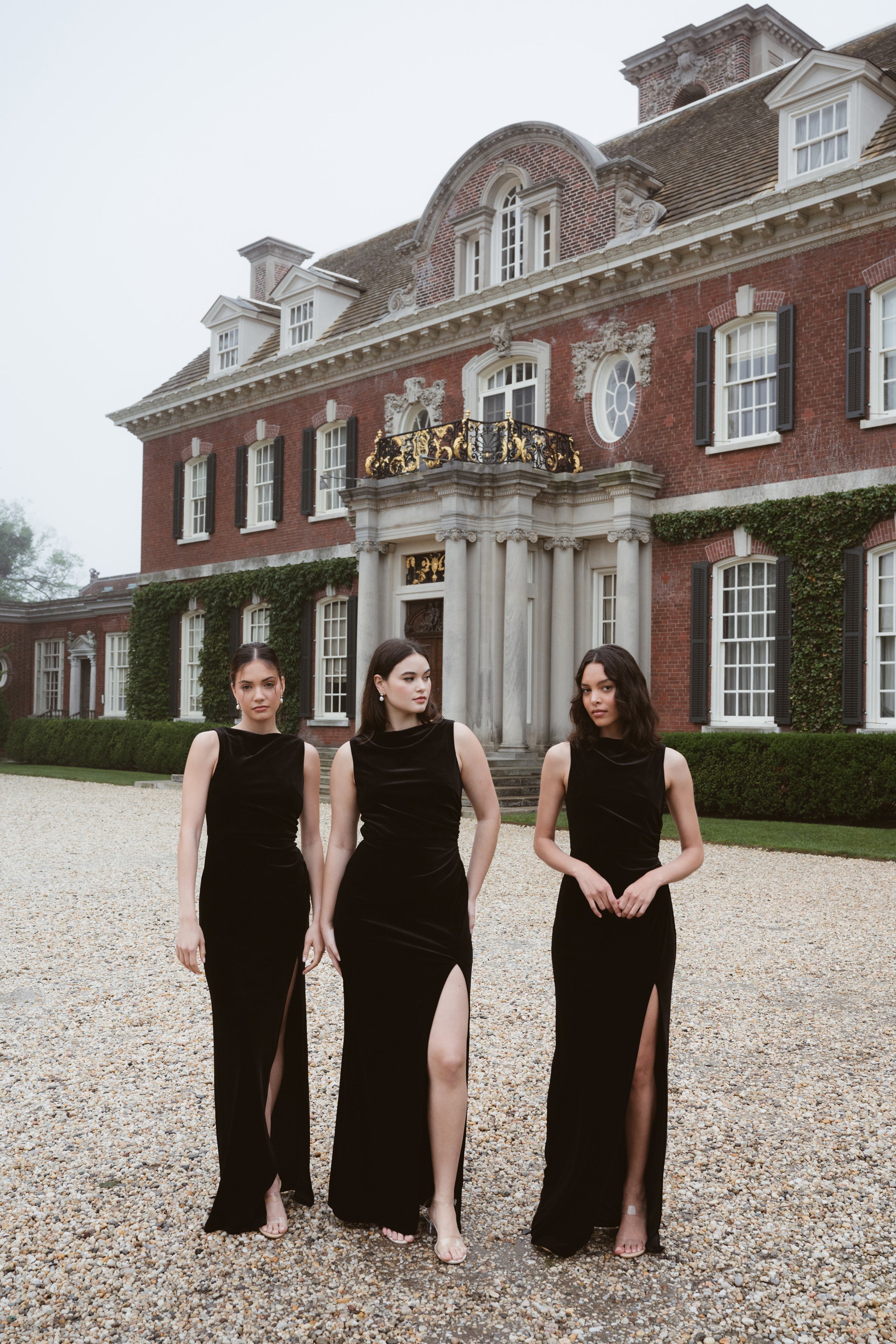 Three bridesmaids wearing black velvet high neck bridal party gowns in front of historic mansion.