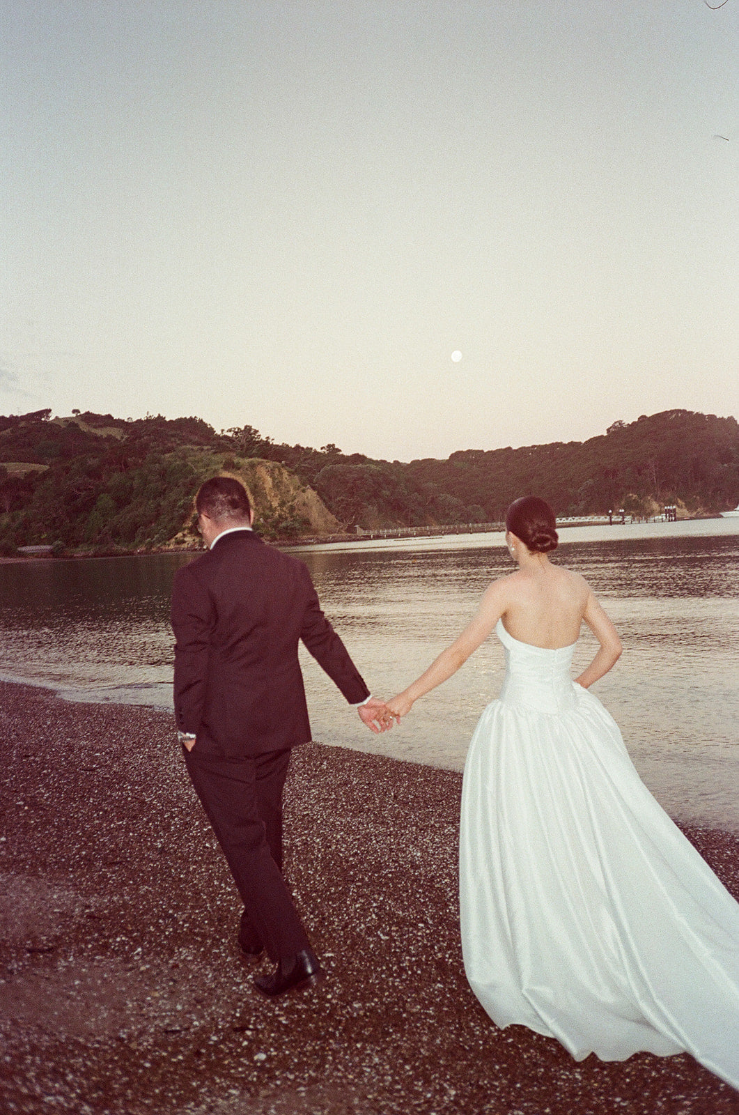 Real bride wearing a draped strapless bodice, drop waist, full a line wedding gown on a beach.