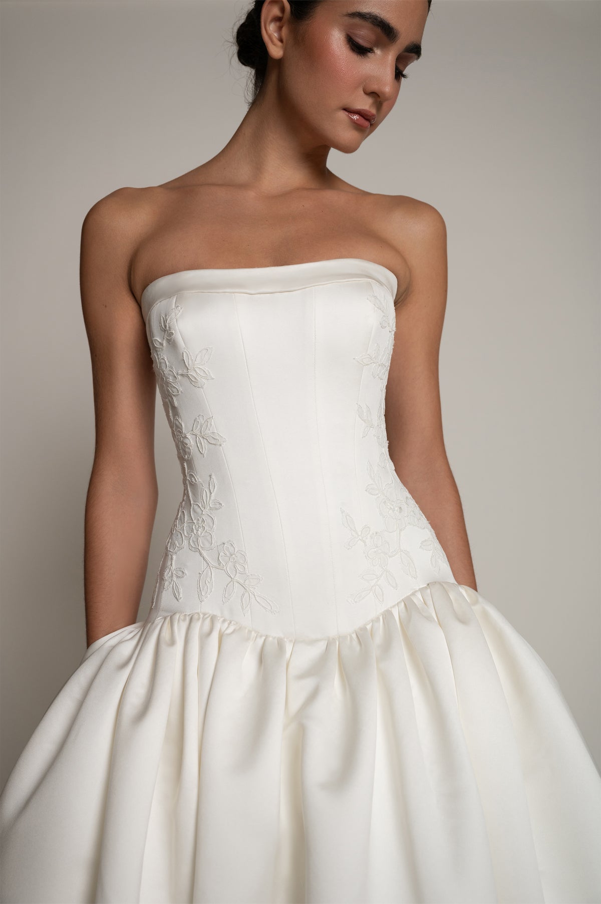 A strapless white wedding gown with a structured corset-style bodice and a voluminous gathered skirt, shown on a model against a plain light gray studio background.