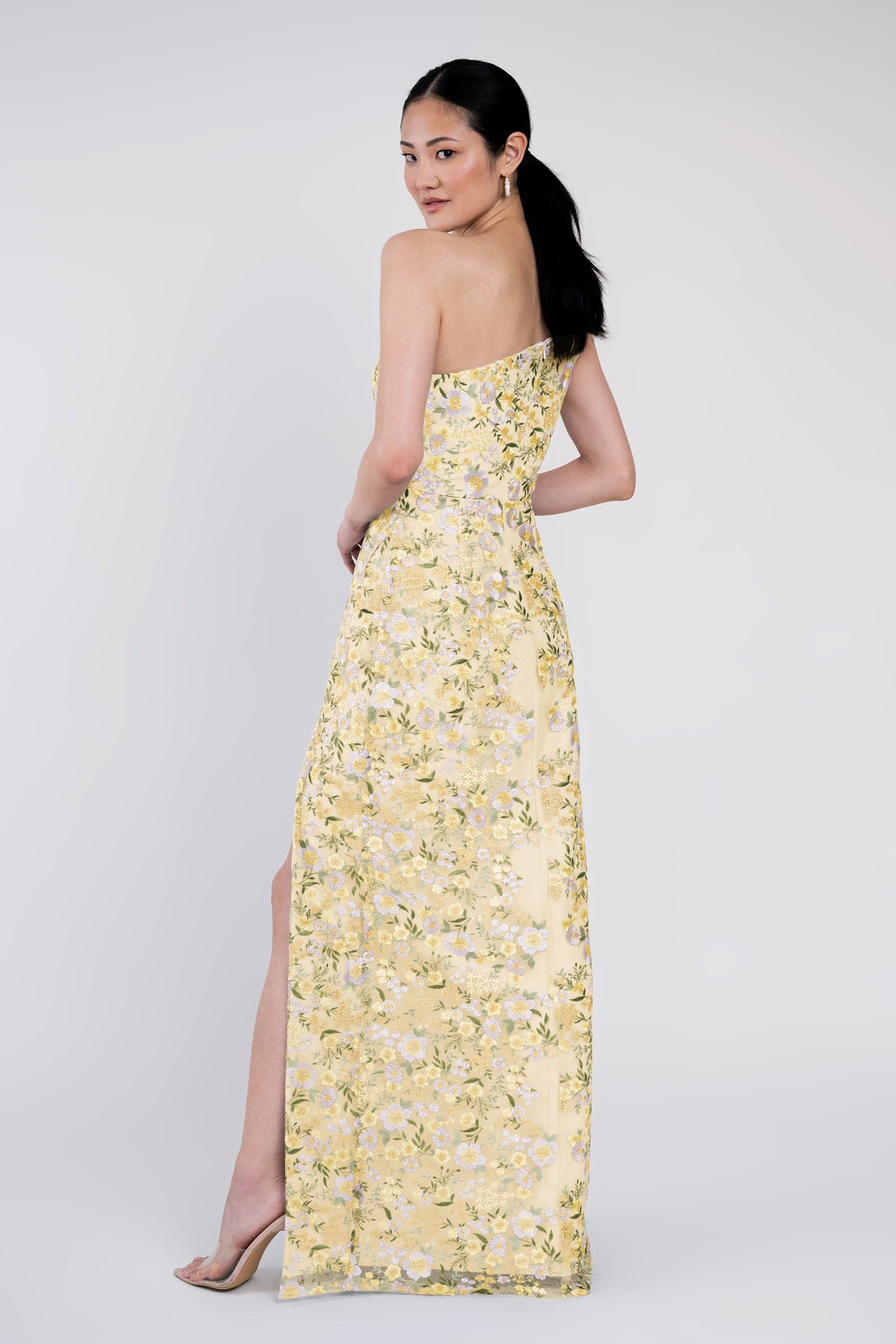 Woman wearing a yellow floral one-shoulder dress on a white background