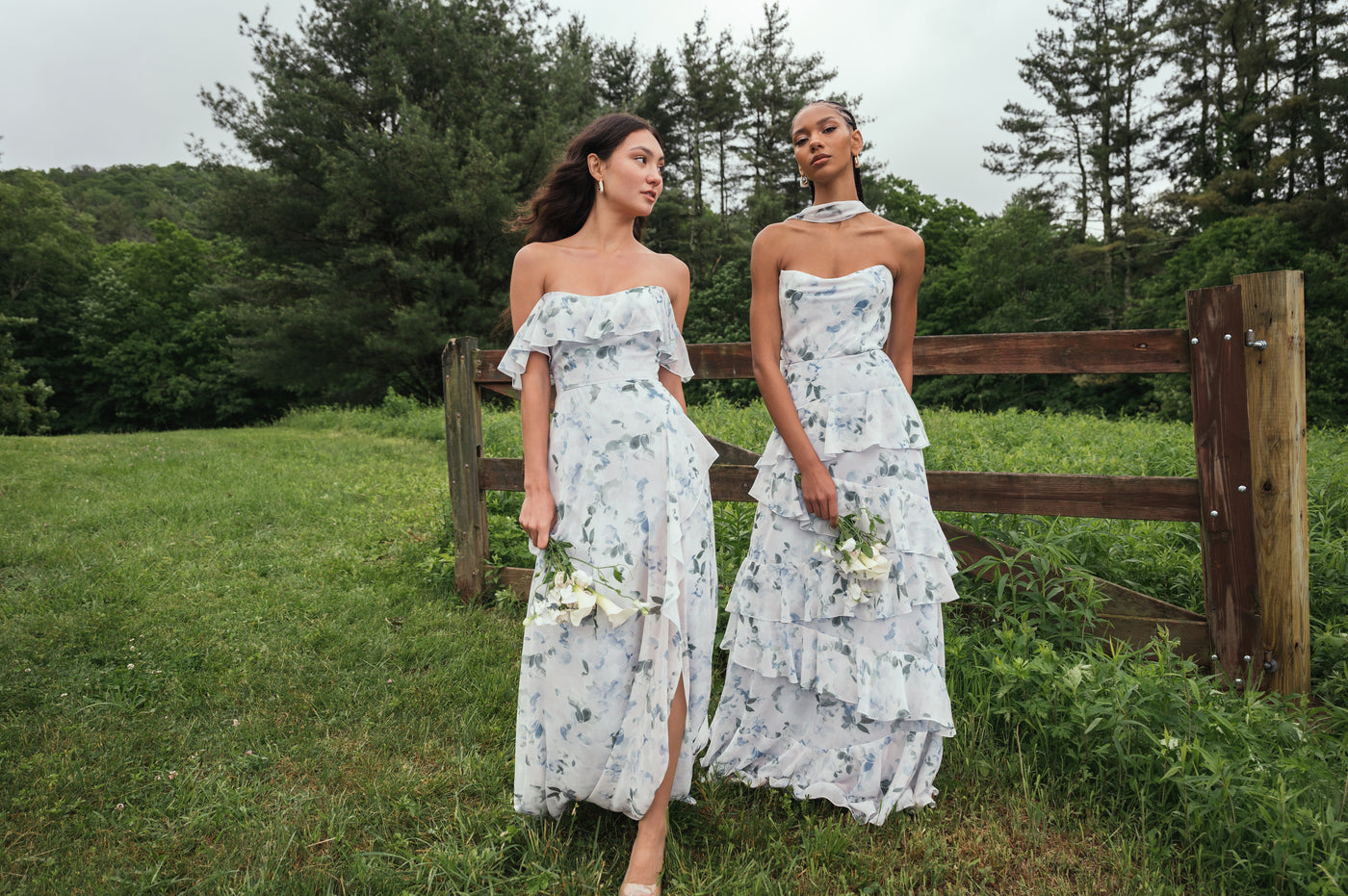 Two bridesmaids outside on green grass wearing printed floral chiffon bridesmaid dresses with ruffles.