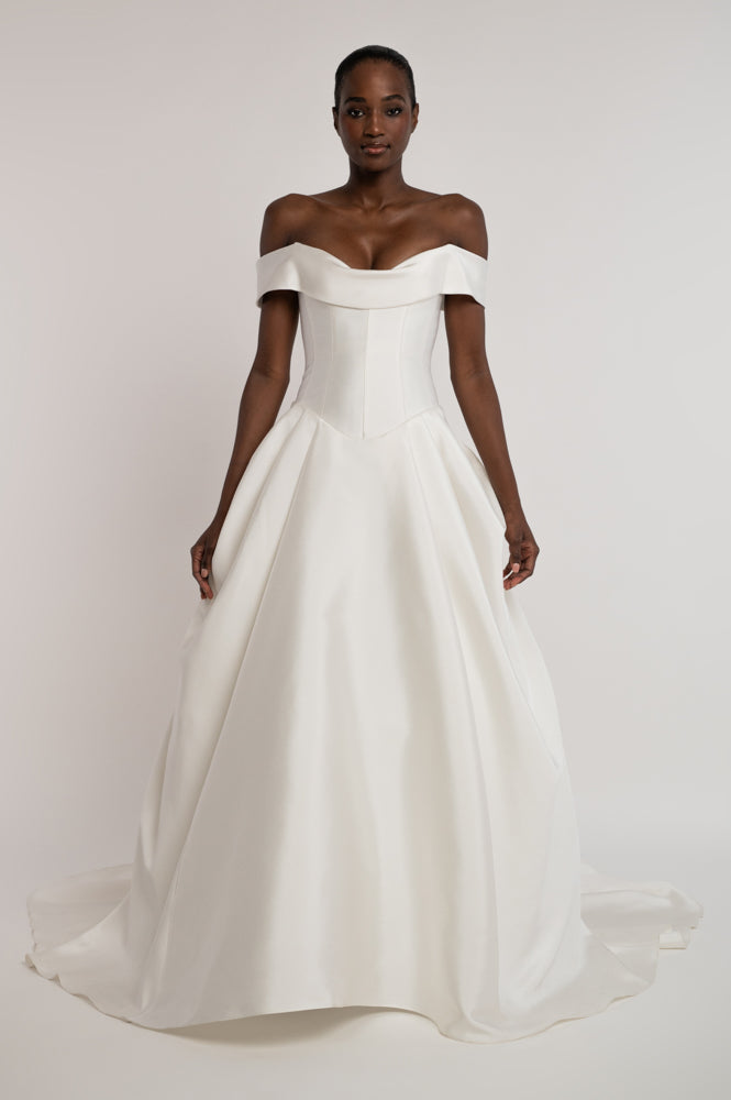 An off-the-shoulder white satin ball gown with a structured corset-style bodice and a full, flowing skirt, shown on a model against a light gray studio background.