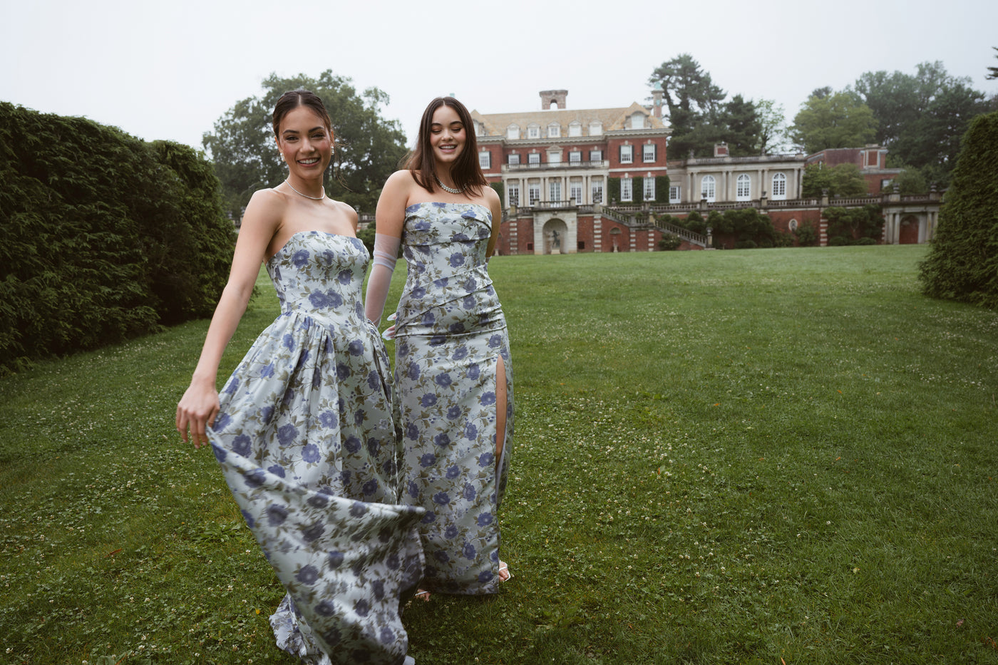 Two bridesmaids in blue floral jacquard bridal party dresses on large green lawn.