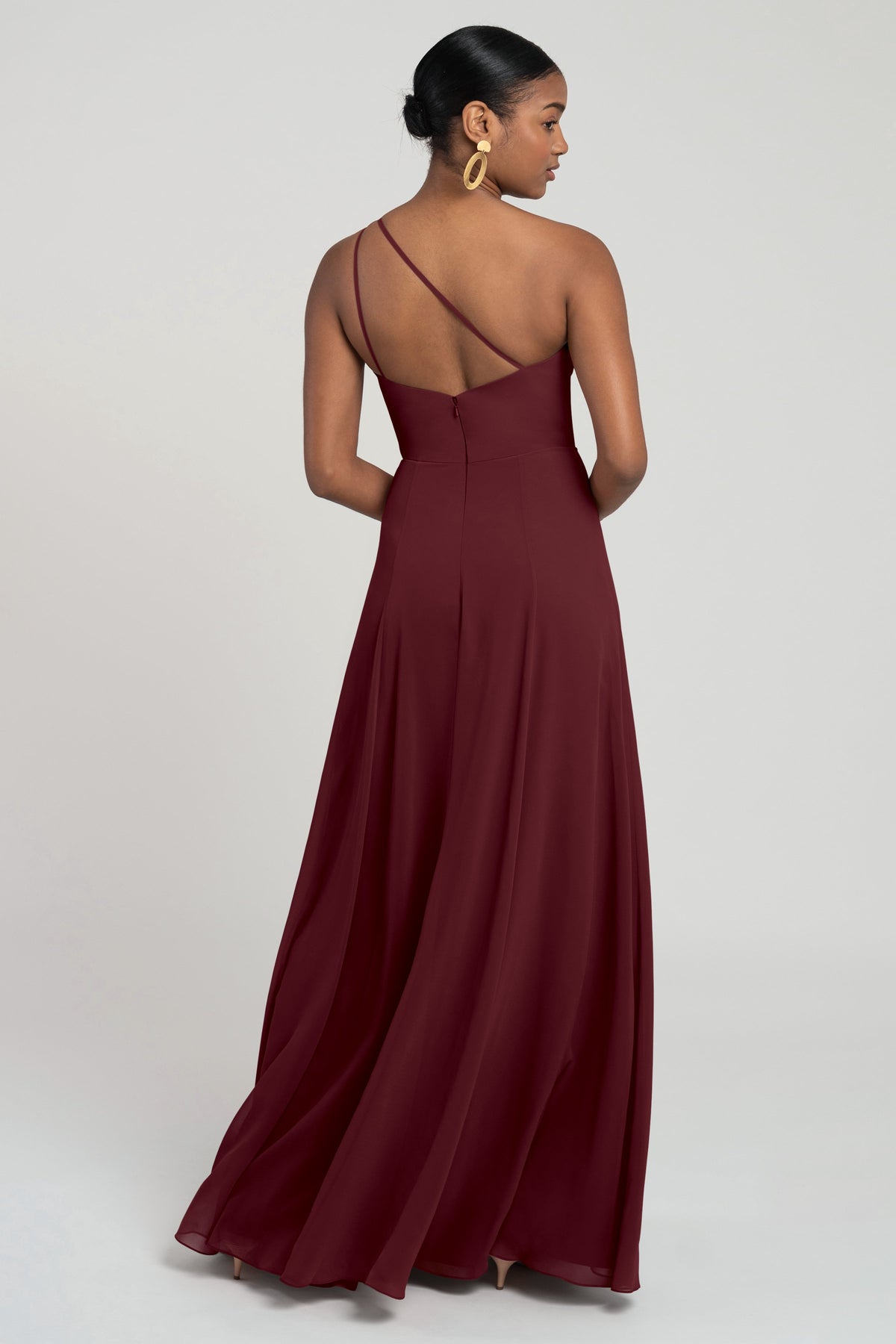 Woman wearing a burgundy evening gown with a backless design on a white background