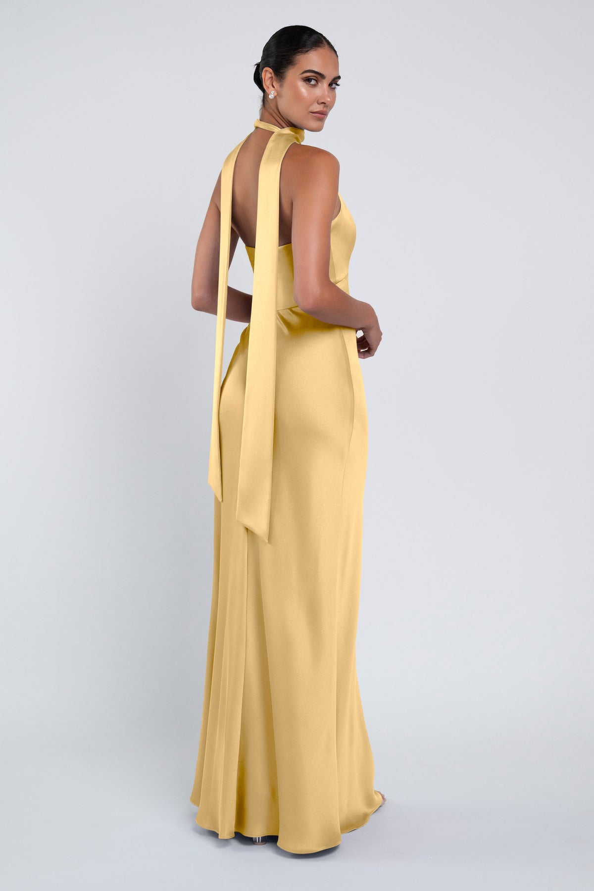 Woman wearing a yellow evening gown with a halter neck design on a light gray background