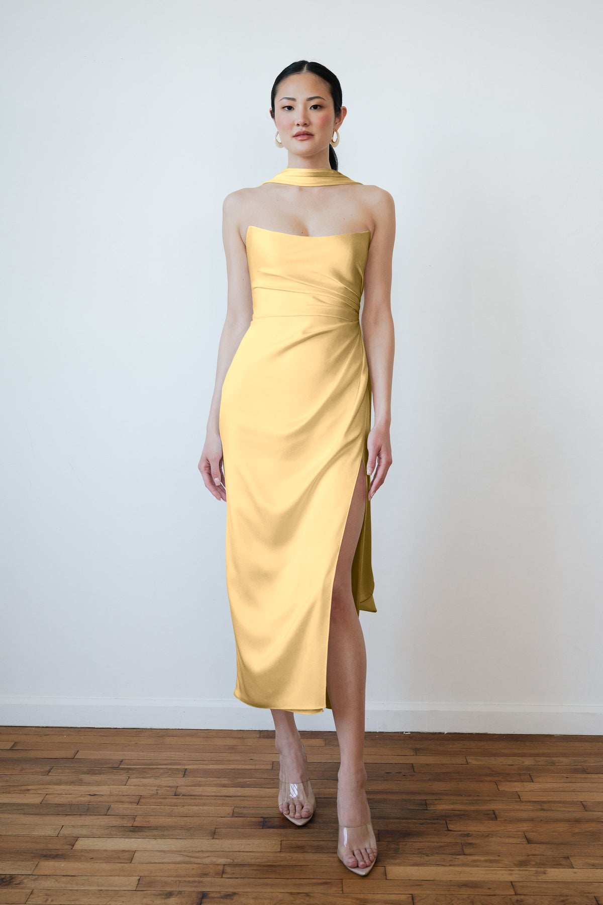 Woman wearing a yellow dress with sheer sleeves against a white wall.