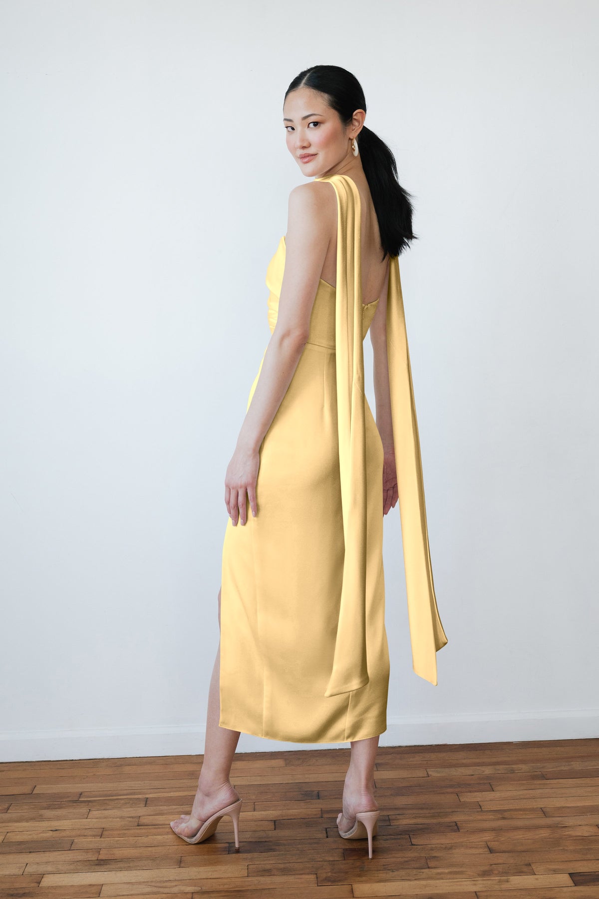 Woman wearing a yellow dress with a long train against a white wall.