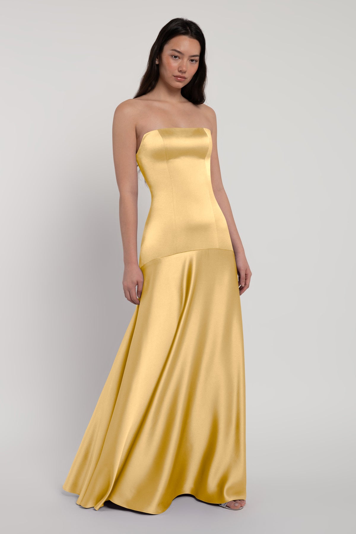 Woman wearing a strapless yellow evening gown on a plain background