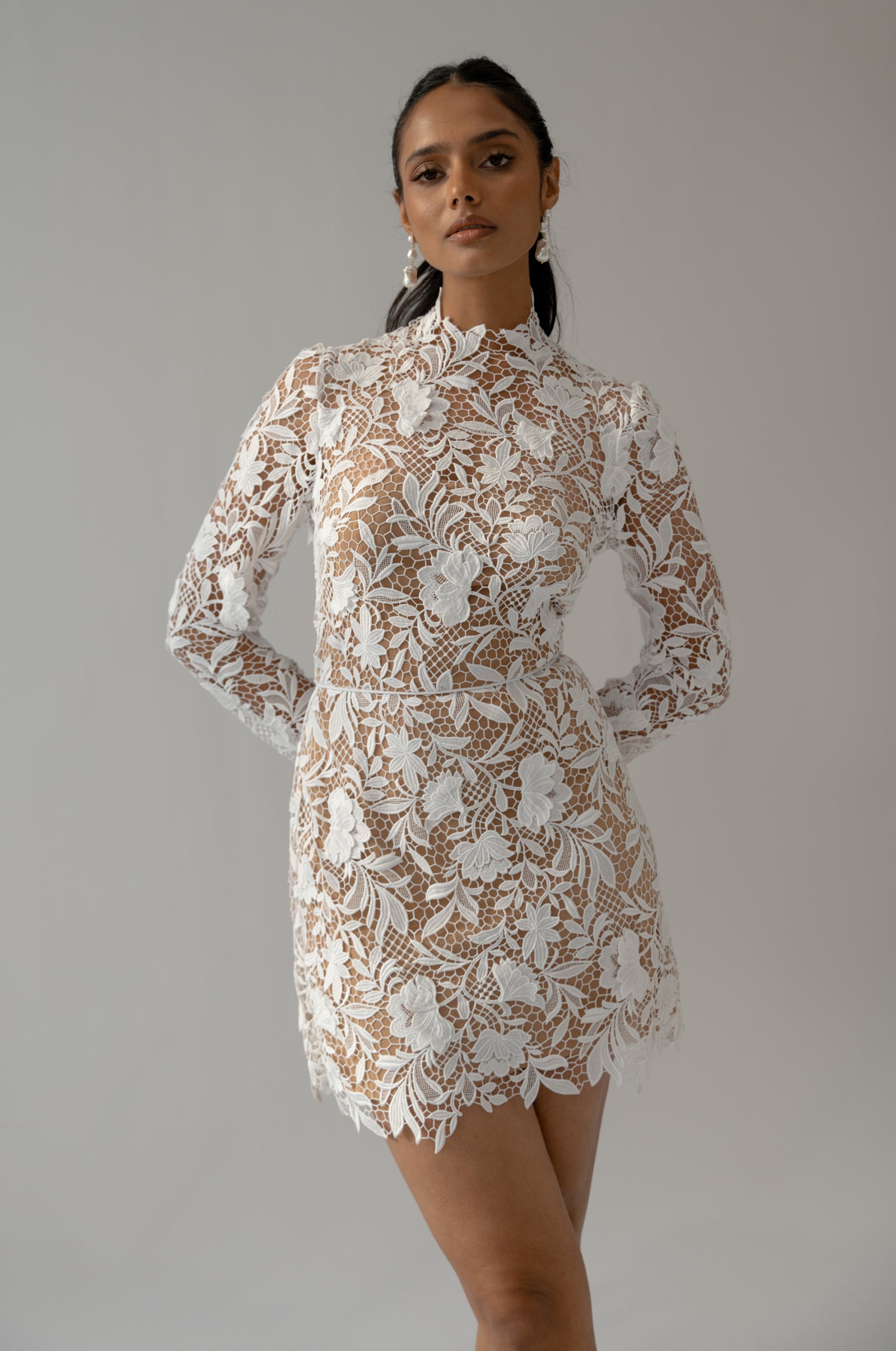 Long sleeve lace mini wedding dress with high neck and short skirt on model.