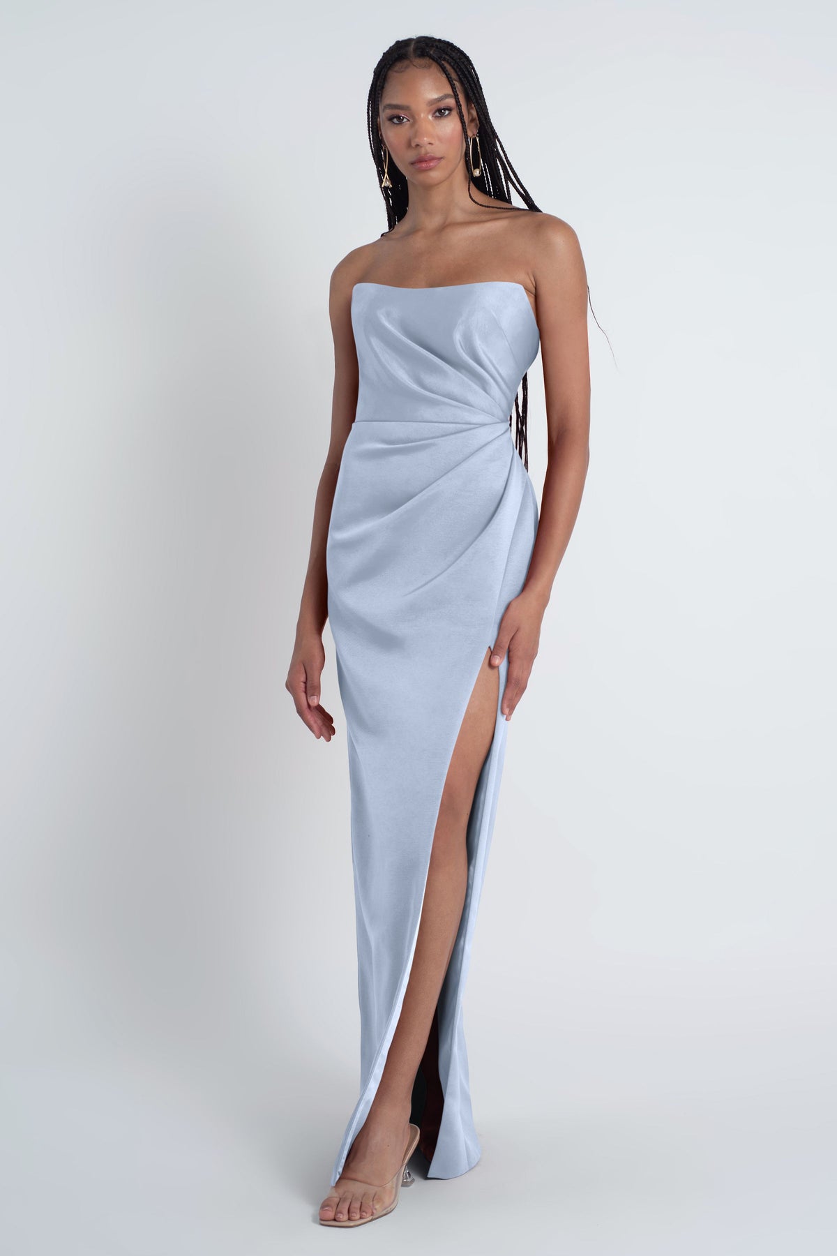 Woman wearing a light blue strapless gown with a high slit on a white background